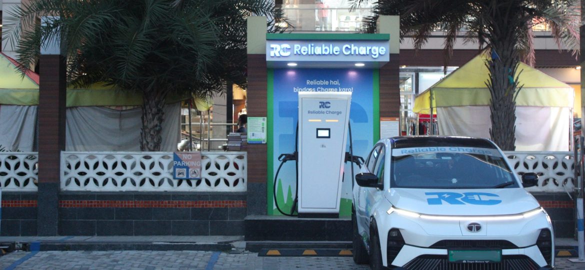 Reliable Charge EV charging station installed outside a shopping complex with palm trees, featuring a white Tata curve electric car parked and charging at the unit.