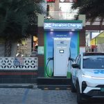 Reliable Charge EV charging station installed outside a shopping complex with palm trees, featuring a white Tata curve electric car parked and charging at the unit.