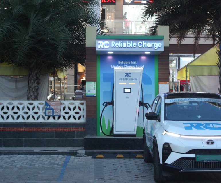 Reliable Charge EV charging station installed outside a shopping complex with palm trees, featuring a white Tata curve electric car parked and charging at the unit.
